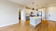 Located at 2307 N Tryon St in Charlotte, NC, this 910-square-foot apartment offers two bedrooms, two bathrooms, and a thoughtfully designed single-level floor plan. The open-concept kitchen and living area serves as the heart of the unit, featuring warm hardwood-style flooring that flows throughout the space. The kitchen is outfitted with white upper cabinetry, gray lower cabinets, a white quartz waterfall island with an undermount sink, and stainless steel appliances including a refrigerator, range, and microwave. A classic white subway tile backsplash and matte black pendant lighting add a contemporary touch. Recessed lighting illuminates the space throughout. The primary bedroom measures 170 square feet, providing a comfortable retreat. Both bedrooms are complemented by dedicated closets, offering ample storage. The unit includes two full bathrooms and a dedicated laundry space for added convenience. A walk-in storage closet is also accessible from the main living area. The overall aesthetic is clean and modern, blending neutral tones with updated finishes throughout.