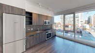 Located in the vibrant Navy Yard neighborhood of Washington, DC, this contemporary residence at 1201 Half St SE showcases a thoughtfully designed single-floor layout with clean lines and modern finishes throughout. Large floor-to-ceiling windows flood the living spaces with abundant natural light while offering dynamic views of the surrounding urban skyline and the evolving DC waterfront district.

The open-concept living and dining area features light hardwood-style flooring and crisp white walls, creating a bright and airy atmosphere. The sleek, modern kitchen is outfitted with wood-grain cabinetry, a gray stone countertop, a glass tile backsplash, and a full suite of stainless steel appliances including an electric range, built-in microwave, and refrigerator — all positioned alongside a generous window that frames city views.

The bedrooms continue the clean aesthetic with neutral tones, hardwood-style floors, and oversized windows. The bathrooms are elegantly appointed with large-format stone-look floor and wall tiles, dark stone vanity countertops, illuminated mirrors, and a full soaking tub with a rain showerhead. Every detail reflects a commitment to contemporary urban living in one of DC's most dynamic and rapidly growing neighborhoods.