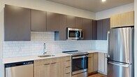 This thoughtfully designed 1-bedroom, 1-bathroom residence offers a clean, modern aesthetic throughout its single-floor layout. Light hardwood flooring flows seamlessly from room to room, complementing the crisp white walls and recessed lighting that brighten the entire space.

The open-concept kitchen and living area serves as the heart of the home. The kitchen is outfitted with a full suite of stainless steel appliances, including a refrigerator, electric range, built-in microwave, and dishwasher. Two-toned cabinetry — featuring light wood lower cabinets and charcoal upper cabinets — pairs elegantly with white quartz countertops and a classic subway tile backsplash. The living area adjoins the kitchen and opens to a private balcony through a glass door, allowing natural light to fill the space.

A long hallway connects the main living area to the private bedroom, which features a ceiling fan, generous natural light from a large window with outdoor views, and a dedicated closet for storage.

The bathroom is finished with a wood-toned vanity, an undermount sink with modern fixtures, a large mirror, and a clean, minimalist design.

Central HVAC, recessed lighting throughout, and contemporary finishes complete this well-appointed residence.