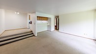 Located at 7003 W Kinnickinnic River Pkwy in Milwaukee, Wisconsin, this single-floor unit offers a functional and well-organized layout across multiple living spaces. The galley-style kitchen is equipped with warm wood cabinetry, white appliances including a gas range and refrigerator, a double basin sink, and light-toned countertops, all set on easy-care vinyl flooring. A pass-through counter connects the kitchen to the main living area, which features plush carpet, a built-in shelving unit, and a large sliding glass door that fills the room with natural light and offers views of surrounding greenery. A separate sunken living room area adds architectural interest, accessible via a few steps. The bedrooms are carpeted and generously sized, each with large windows dressed in vertical blinds that frame outdoor tree views, and include wall unit air conditioning and baseboard heating. Closet space is provided via bifold-door closets. The unit includes two full bathrooms — one featuring mosaic tile surround on the tub/shower combination, and another with a clean white tub/shower unit and mosaic tile flooring. The overall ambiance is bright and neutral, with a practical design suited for comfortable everyday living.