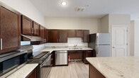 This single-story unit offers four bedrooms and two bathrooms across a thoughtfully designed floor plan. The kitchen serves as a central highlight, featuring rich dark-brown cabinetry, granite countertops, a white subway tile backsplash, and a central island with additional granite workspace. Stainless steel appliances — including a refrigerator, gas range, dishwasher, and microwave — complete the kitchen's functional and modern aesthetic. The kitchen flows into the adjacent living area, which features light hardwood-style flooring and neutral beige walls that carry consistently throughout the unit. Each bedroom is finished with the same light flooring, ceiling fans in select rooms, and windows with blinds allowing natural light. The primary bedroom offers a modest but comfortable footprint. Two closets provide dedicated storage, featuring wire shelving systems. The two bathrooms are finished with granite-topped dark vanities, large-format tile flooring, and glass-enclosed walk-in showers with white subway tile surrounds, maintaining a clean and cohesive design throughout the unit.