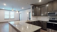 This single-floor residence showcases a cohesive, modern design throughout. The kitchen serves as a central highlight, featuring an expansive granite-topped peninsula with an undermount sink, dark espresso-toned cabinetry with brushed nickel hardware, and a full suite of stainless steel appliances including a refrigerator, range, and over-the-range microwave. A white subway tile backsplash adds contrast, while pendant lighting above the peninsula provides both task and ambient illumination. Recessed lighting and crown molding add a polished finish to the open-concept kitchen and living area.

The bedrooms are generously proportioned, each featuring wood-look plank flooring, neutral-toned walls, dark baseboards and trim, ceiling fans, and blinds-fitted windows that allow ample natural light. The layout includes multiple bedrooms, offering flexible living arrangements.

Both bathrooms mirror each other in design, each presenting a double-vanity with granite countertops, dark cabinetry, a large framed mirror, and a tub-shower combination. Wood-look flooring extends throughout, maintaining design consistency. A walk-in closet is accessible from one of the bathrooms, adding practical storage.