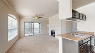 Located in Plano, TX, this two-bedroom, one-bathroom residence offers a well-designed single-floor layout that balances comfort and functionality. The open-concept living and dining area is a welcoming centerpiece, featuring plush carpet, crown molding, a ceiling fan, and a classic fireplace flanked by built-in shelving. Sliding glass doors lead to a private balcony, flooding the space with natural light and offering pleasant outdoor views. The kitchen is thoughtfully appointed with dark cabinetry, granite-style countertops, a mosaic tile backsplash, black appliances including a refrigerator and range, and a peninsula with a sink that opens to the living area. Rich hardwood-style flooring runs through the kitchen and hallway, complementing the carpet in the living and bedroom areas. The primary bedroom is generously sized with vaulted ceilings, a ceiling fan, and access to a dedicated walk-in closet. The second bedroom also features vaulted ceilings, a ceiling fan, and a large window that allows ample natural light. The bathroom is clean and functional, offering a combination tub and shower with sliding glass doors, a dark-cabinetry vanity with a white sink, and wood-look tile flooring. A hallway with crown molding connects all rooms seamlessly.