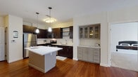 Located on Upland Woods Circle in Norwood, MA, this single-floor residence offers a thoughtfully designed layout with modern finishes throughout. The kitchen is a standout feature, showcasing rich dark cabinetry, stainless steel appliances including a gas range, microwave, dishwasher, and refrigerator, all complemented by crisp white countertops and a subway tile backsplash. A central island provides additional prep space, while stylish pendant lighting adds a contemporary touch. Adjacent to the kitchen, a built-in hutch with glass-front cabinetry offers additional storage and display space. Warm hardwood flooring flows through the kitchen and living areas, while plush carpeting adds comfort to the bedrooms. The generously sized bedroom features a ceiling fan, large windows that invite natural light, and access to a spacious walk-in closet with wire shelving. Two bathrooms serve the residence, each finished with large-format tile flooring and dark vanity cabinetry with clean white countertops. The living area benefits from a sliding glass door that opens to an outdoor space, allowing ample natural light to fill the room. The overall ambiance is clean, modern, and move-in ready.
