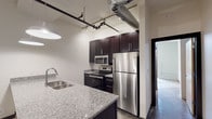 Located at 711 S Lexington Ave in Burlington, North Carolina, this single-floor unit showcases a compelling industrial aesthetic carried throughout its open layout. Exposed metal ductwork and pipe-style track lighting run along the ceilings, lending a loft-like character to the living spaces. Polished and raw concrete floors ground the interiors with an urban, warehouse-inspired feel.

The kitchen is a standout feature, equipped with rich dark cabinetry, granite countertops, and a full suite of stainless steel appliances including a refrigerator, electric range, and built-in microwave. A spacious kitchen island with a double undermount sink and pendant lighting overhead makes the space as functional as it is visually striking.

The open living area is generously proportioned, benefiting from ceiling fans and recessed and wall-mounted lighting that illuminate the expansive, unobstructed floor plan — ideal for flexible furniture arrangements or multi-use configurations.

The bathrooms mirror the design language of the kitchen, featuring dark wood vanities topped with matching granite countertops and chrome hardware. Each bathroom includes a full tub-shower combination with a curved chrome curtain rod, recessed lighting, and clean white surrounds. The overall ambiance of the unit blends modern finishes with raw industrial elements for a distinctive and contemporary living environment.