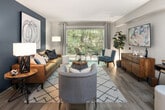 This single-story residence offers a thoughtfully designed layout across three bedrooms and two full bathrooms. The open-concept living room is a standout space, featuring wood-style plank flooring, a bold teal accent wall, and a large sliding glass door that floods the room with natural light while providing views of surrounding greenery. The adjoining dining area is defined by a pendant light fixture and flows seamlessly into the kitchen, which is equipped with stainless steel appliances, two-tone gray and white cabinetry, granite-style countertops, and a window above the sink for additional natural light.

The bedrooms maintain a consistent, calming aesthetic with soft gray walls, wood-style flooring, and ample closet space. The primary bedroom receives natural light through large windows with outdoor views. Both bathrooms are finished with granite-topped gray vanities, tiled tub-shower combinations, and wood-look flooring, lending a clean, contemporary feel. Connecting hallways provide efficient circulation throughout the home. Overall, the space presents a cohesive modern design with neutral tones, quality finishes, and a functional, comfortable layout.