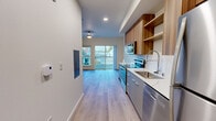 This single-floor unit at 633B SW 150th St, Unit 6 in Burien, Washington presents a thoughtfully designed contemporary living space with clean lines and modern finishes throughout. Light wood-tone flooring runs continuously across the entire unit, creating a cohesive and airy feel.

The kitchen serves as a functional centerpiece, featuring stainless steel appliances including a range, microwave, dishwasher, and refrigerator. Two-tone cabinetry pairs warm wood upper cabinets and open shelving with sleek gray lower cabinets, complemented by white quartz countertops and a stainless steel sink with a flexible pull-down faucet. Recessed lighting illuminates the workspace effectively.

The living area is generously proportioned, bathed in natural light from large sliding glass doors that open to a private balcony with metal railings and outdoor views of the surrounding Burien neighborhood. A ceiling fan provides added comfort.

The bedroom offers a quiet, open layout with neutral white walls and access to natural light. The bathroom maintains the unit's modern aesthetic with gray cabinetry, a white vanity countertop, and light wood-tone flooring. A closet with built-in shelving provides practical storage. The unit also includes an in-unit utility area, adding everyday convenience to this well-appointed space.