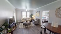 Located at 915 Desco Ln in Grand Prairie, Texas, this single-story home offers a well-designed layout with consistent dark hardwood-style flooring and a neutral gray palette throughout. The living area serves as the heart of the home, featuring crown molding, a ceiling fan, and multiple windows dressed with patterned curtains that invite generous natural light. A side door provides convenient exterior access directly from the living space. The galley-style kitchen is efficiently organized with white cabinetry, granite-look countertops, a double stainless steel sink, and white appliances, including a range and refrigerator. Ample upper and lower cabinet storage lines both sides of the kitchen. The primary bedroom is a bright, comfortable retreat with large windows overlooking the outdoors and a ceiling fan overhead. It connects to a private bathroom featuring a white vanity with granite-look countertops, and a walk-through passage leading to a dedicated walk-in closet. A second bedroom also benefits from natural light through dual windows. The bathrooms maintain a clean, classic aesthetic with tiled tub-shower combinations and white vanities. Crown molding in the main living areas adds an elevated architectural touch throughout this well-appointed home.