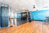 Located at 1352 Randolph Road in Plainfield, NJ, this single-floor fitness center is designed to accommodate a comprehensive range of workout activities within a clean, modern environment. The space is organized into distinct functional zones, each tailored to specific training needs.

The cardio area features warm hardwood flooring and is equipped with treadmills, elliptical machines, and rowing machines. Pendant-style industrial lighting hangs from a drop-tile ceiling, lending a contemporary aesthetic, while multiple windows along the perimeter allow natural light to fill the space and provide views of the surrounding area.

The strength training zone transitions to rubberized flooring for safety and functionality, and includes a Smith machine, weight bench, cable stations, and additional resistance equipment. A striking teal accent wall bearing fitness-themed typography — including words like "Strong," "Fit," "Endurance," and "Nutrition" — serves as a bold visual focal point.

A dedicated open-floor studio area, enclosed by glass partition walls, offers a versatile space suitable for group classes, stretching, or functional training. Motivational wall graphics with phrases such as "No Excuses" and "Focus" reinforce the energetic atmosphere throughout. The overall design balances functionality with an inviting, motivating ambiance.