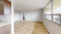 Located at 288 Mount Albion Rd in Hamilton, Ontario, this well-appointed two-bedroom, one-bathroom unit offers a comfortable and functional layout with consistent light hardwood flooring throughout. The galley-style kitchen is lined with warm walnut-toned cabinetry on both sides, providing generous storage and counter space, complemented by a stainless steel sink and light stone countertops. The kitchen flows seamlessly into a spacious, light-filled living area featuring large windows and access to a glazed balcony that captures sweeping panoramic views of the surrounding cityscape and beyond. Both bedrooms are well-proportioned; the primary bedroom features a ceiling fan and a full-width sliding wood-panel closet, while the second bedroom also includes built-in closet storage, a ceiling fan, and a bright window with outdoor views. Baseboard heating is present throughout the unit. The full bathroom is finished with white subway tile surrounding a soaker tub and shower combination, a wood-toned vanity, and hardwood flooring. A dedicated hallway connects all rooms, contributing to a logical and efficient floor plan. The unit's clean, neutral palette and consistent finishes create a bright, cohesive ambiance throughout.