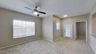 This single-floor residence offers a well-designed, open-concept layout that seamlessly connects the kitchen and living areas. The kitchen is a functional highlight, featuring granite countertops, white shaker-style cabinetry, stainless steel appliances including a refrigerator, electric range, and built-in microwave, as well as wood-look flooring that adds warmth and durability. A breakfast bar provides a natural transition into the carpeted living area, which is enhanced by a ceiling fan with light and access to the exterior via a door with sidelights that invite natural light. The spacious living room offers multiple windows fitted with white blinds, creating a bright and airy atmosphere. The bedrooms are generously sized, each equipped with ceiling fans and plush carpeting. Closet space is well-provided, with at least one bedroom featuring a walk-in closet. Both bathrooms are finished with granite-top vanities, white cabinetry, wood-look flooring, and tub-shower combinations, offering a clean and cohesive aesthetic. Neutral taupe wall tones are consistent throughout the residence, contributing to a calm, move-in-ready environment. The overall layout is practical and comfortable, suited for everyday living.