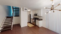 Located in Valley Village along Radford Avenue in Los Angeles, this two-story residence blends mid-century architectural character with modern updates throughout. Rich, dark hardwood flooring flows consistently across both levels, anchoring the home's warm yet contemporary aesthetic.

The lower level opens to a well-appointed kitchen featuring white shaker cabinetry, dark countertops, and a full suite of stainless steel appliances including a refrigerator, electric range, and over-the-range microwave. An adjacent dining area benefits from natural light filtering through vertical blinds and is accented by a stylish sputnik chandelier. A striking freestanding yellow fireplace set on a terracotta tile hearth serves as a bold focal point in the living area, complemented by exposed wood-beam ceilings that lend the space a distinctive mid-century character.

The upper level continues the exposed beam and wood-plank ceiling detail, creating a warm, cabin-like ambiance in the bedroom spaces. One bedroom features floor-to-ceiling mirrored closet doors and large windows dressed with vertical blinds that allow ample natural light. The bathroom is finished with white cabinetry, a quartz-topped vanity, generous built-in storage, and a large mirror. A staircase with ornamental iron railings connects both floors, adding an elegant architectural detail to the overall design.