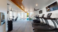 Located at 4000 Revere Blvd in Sherrills Ford, NC, this single-floor fitness center is thoughtfully designed to accommodate a wide range of workout styles and fitness goals. The space is divided into distinct functional zones, each outfitted with professional-grade equipment.

The cardio area features a row of TRUE treadmills and stationary bikes, positioned beneath wall-mounted flat-screen televisions and a ceiling fan that keeps the environment comfortable during intense workouts. A warm wood-paneled ceiling detail adds a refined architectural touch, contrasting beautifully with the crisp white walls and neutral carpet flooring.

A glass-partitioned studio area provides a flexible space for stretching, group workouts, or yoga sessions. It is equipped with stability balls in various sizes, resistance bands, medicine balls, and exercise mats, all neatly organized on a freestanding rack. Large windows flood this zone with natural light and offer views of the surrounding area.

Adjacent to the studio, a dedicated strength training room features rubber flooring, a multi-function cable machine, a dumbbell rack, kettlebells, a weight bench, and a rowing machine. Mirrors line the walls to support proper form, and ample natural light from multiple windows creates an energizing atmosphere. A small activity nook near the treadmill area adds a thoughtful, family-friendly touch to the overall layout.