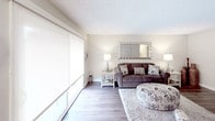 This single-floor residence offers a thoughtfully arranged layout across several interconnected living spaces. The living room provides a comfortable gathering area with hardwood-style flooring, neutral warm-toned walls, a textured ceiling, and large windows fitted with roller shades that allow for controlled natural light. The space accommodates a seating arrangement centered around a wall-mounted television, with an open sightline into the hallway beyond.

The adjacent kitchen features white cabinetry with brushed nickel hardware, granite-style countertops, and a gas range, with a window offering additional natural light. The dining area nearby includes a ceiling fan with a light fixture and a window with blinds, creating a bright and functional mealtime space.

Two bedrooms are present, each carpeted and featuring textured ceilings and closet access. The primary bedroom includes an open closet area and an en-suite bathroom with a wide vanity, large mirror, and ample under-counter storage. A second full bathroom is also available, equipped with a shower-tub combination and a single-sink vanity with white cabinetry. Hardwood-style flooring carries through the main living areas, contributing to a cohesive and clean aesthetic throughout the unit.