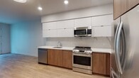 Located at 1738 N Las Palmas Ave in Los Angeles, this single-floor unit showcases a clean, contemporary design throughout. The kitchen is a standout feature, outfitted with two-tone cabinetry — flat-panel white upper cabinets paired with warm wood-grain lower cabinets — complemented by white quartz countertops and a marble-style backsplash. Stainless steel appliances, including a range, over-the-range microwave, dishwasher, and refrigerator, complete the space. Light hardwood-style flooring extends throughout, unifying the kitchen with the open living area, which benefits from recessed lighting and access to a private outdoor space via French doors. The bedroom is bright and airy, featuring a tall window that brings in natural light and views of the surrounding neighborhood. The bathroom is finished with large-format tile flooring, a wood-vanity with white quartz countertop, an undermount sink, and a generously sized LED-backlit mirror, lending a sleek, modern feel. Overall, the unit offers a cohesive, contemporary aesthetic with quality finishes in the heart of Hollywood.