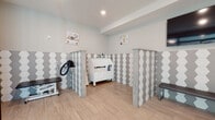 This thoughtfully designed pet grooming facility offers a clean, modern environment purpose-built for the care and comfort of pets and their owners. The space is anchored by a striking aesthetic defined by bold grey-and-white hexagonal tile wainscoting that lines the walls throughout, creating a cohesive and visually engaging look while providing a durable, easy-to-clean surface ideal for a grooming environment.

The grooming area features multiple dedicated stations, each defined by tiled partition columns that offer functional separation between workspaces. A raised pet bathing tub serves as a central fixture, accompanied by a professional-grade pet dryer, grooming tables, and seating benches for waiting clients. Recessed lighting illuminates the space evenly, while playful pet-themed artwork adorns the walls, adding warmth and personality to the interior.

A wall-mounted flat-screen display is positioned for client viewing, and large floor-to-ceiling glass entry doors flood the reception zone with natural light, creating a bright and inviting welcome. The flooring transitions seamlessly between wood-look tile and polished marble-effect tile in the entry area, reinforcing the facility's attention to design detail.

Overall, the space balances practicality with a polished, professional aesthetic, offering a well-equipped and welcoming environment for a full-service pet grooming operation.
