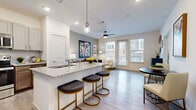 This thoughtfully designed one-bedroom, one-bathroom residence offers an efficient and stylish single-floor layout. The open-concept kitchen and living area serves as the heart of the home, anchored by a granite-topped peninsula with bar seating — ideal for casual dining or entertaining. The kitchen is outfitted with stainless steel appliances, including a full-size refrigerator, range, microwave, and dishwasher, complemented by two-tone cabinetry in gray and warm wood tones, a subway tile backsplash, and recessed lighting with pendant accents. Light wood-style flooring runs throughout, lending a clean, cohesive look to the space. The living room is bright and airy, with large windows and a glass-paneled door that invite abundant natural light and outdoor views. A ceiling fan adds comfort to both the living area and the spacious bedroom. The bedroom features a generous walk-in closet with built-in wire shelving for organized storage. The bathroom includes a deep soaking tub with a tiled surround and overhead shower. Clean white walls, neutral finishes, and a modern aesthetic define the overall ambiance of this well-proportioned residence.