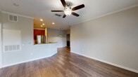 This single-story residence features a well-designed open-concept layout that seamlessly connects the living area to the kitchen. The spacious living room is finished with rich hardwood flooring, crown molding, and a ceiling fan, creating a comfortable and polished atmosphere. Recessed lighting and a decorative pendant light illuminate the transition into the kitchen area.

The kitchen is equipped with rich cherry-toned cabinetry extending to the ceiling, granite countertops, and a full suite of stainless steel appliances including a range, over-the-range microwave, and French door refrigerator. A wraparound breakfast bar with granite countertop provides additional workspace and casual dining space. Light ceramic tile flooring grounds the kitchen zone.

The bedroom is carpeted and generously sized, featuring a ceiling fan with light fixture and a window fitted with blinds that allows natural light into the space.

Two bathrooms are present, each showcasing granite-topped vanities with rich wood cabinetry. The primary bathroom includes a walk-in shower, while the secondary bathroom features a tub-shower combination with glass sliding doors. Both are finished with light ceramic tile flooring. A dedicated utility closet houses the water heater, providing practical storage separation.