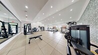 Located at 100 Leslie Oaks Dr in Lithonia, Georgia, this well-appointed fitness center offers a comprehensive exercise facility across a single, expansive floor. The space is designed to accommodate a wide range of workout routines, with clearly defined zones for both cardio and strength training.

The cardio area is lined with multiple treadmills, elliptical trainers, a rowing machine, and stationary bikes, all arranged to take advantage of the natural light streaming in through a series of large windows. Framed artwork adorns the bright white walls, adding a polished, welcoming aesthetic to the environment.

The strength training section features a multi-functional cable and weight machine, a power rack, adjustable benches, and a dumbbell rack, providing ample options for resistance workouts. Full-length mirrors span entire wall sections, visually expanding the space and allowing users to monitor their form during exercise.

Underfoot, a combination of large-format tile and rubberized flooring provides both durability and safety throughout the facility. Recessed lighting illuminates the entire space evenly, complementing the natural light. An accent wall featuring a bold botanical wallpaper adds a contemporary design touch. The overall ambiance is clean, modern, and energizing — well-suited for a community fitness facility.