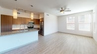 This thoughtfully designed single-floor residence offers a clean, contemporary aesthetic with consistent finishes carried throughout each room. The open-concept kitchen serves as the centerpiece of the living area, featuring warm wood-tone cabinetry with brushed hardware, granite countertops, a large central island with an undermount sink and a flexible pull-down faucet, and a full suite of stainless steel appliances including a range, microwave, and refrigerator. Track lighting and pendant fixtures illuminate the kitchen, while light-toned luxury vinyl plank flooring extends into the adjoining living space. The living area is generously proportioned, benefiting from natural light through large windows and a ceiling fan overhead. A door provides access to a private balcony or patio. The two bedrooms are finished with plush wall-to-wall carpeting and include windows that bring in natural light. The primary bedroom connects directly to its own bathroom and a walk-in closet. Both bathrooms are finished with granite-topped vanities featuring wood cabinetry, undermount sinks, framed mirrors, and tile-look flooring. Grab bars are thoughtfully incorporated in each bathroom, reflecting an accessibility-conscious design. Overall, the space presents a bright, neutral palette with modern materials that create a clean and livable environment.