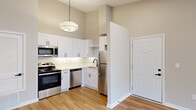 Located at 1500 Champions Pines Lane in Augusta, Georgia, this 1-bedroom, 2-bathroom residence offers a clean, modern aesthetic throughout its efficiently organized single-floor layout. The kitchen is a standout feature, showcasing white shaker-style cabinetry with matte black hardware, a white subway tile backsplash, stainless steel appliances including a range, microwave, dishwasher, and refrigerator, and light wood-tone flooring that extends throughout the main living areas. A stylish pendant light adds a finishing touch overhead. The living area benefits from natural light streaming through French doors fitted with blinds, creating a bright and inviting atmosphere. The bedroom is carpeted for comfort, features vaulted ceilings with a ceiling fan, and includes a window with outdoor views. Both bathrooms are finished with white vanities, matte black fixtures, round mirrors, and a clean tile aesthetic; one includes a tub-shower combination with white vertical tile surround. A dedicated closet provides additional storage. Neutral wall tones and consistent finishes throughout create a cohesive and contemporary feel, making this a well-designed and functional residence.