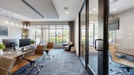 Located at 770 N Eldridge Pkwy in Houston, TX, this single-floor professional office space offers a thoughtfully designed environment suited for productivity and collaboration. The layout comprises two offices, a conference center, and a dining room, all unified by consistent blue-toned patterned carpet flooring and a clean, contemporary aesthetic.

The main office area is bright and open, featuring expansive floor-to-ceiling windows that flood the space with natural light and provide views of the surrounding landscaped exterior. Granite-topped desks paired with ergonomic leather chairs and teardrop pendant lighting create a polished, functional workstation environment. A seating area with a lounge chair offers a comfortable informal setting within the same open space.

The dedicated conference center, accessible through sleek glass-panel doors, is anchored by a substantial wooden conference table surrounded by cushioned rolling chairs. A modern linear chandelier illuminates the room, while curated artwork adorns the walls, adding a refined touch. A private office features warm gray walls, rich wood cabinetry with granite countertops, and carefully selected framed artwork, offering a quiet, executive-style workspace. Large windows throughout provide views of the stone exterior facade. The space is accessed via glass-framed entry doors, reinforcing the modern, professional character of the overall design.