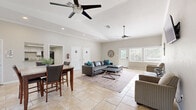 Located at 11300 Mesa Dr in Little Rock, Arkansas, this single-floor space offers an efficiently designed open-concept layout that maximizes its footprint. The interior is unified by large-format travertine-style tile flooring throughout, creating a cohesive and clean aesthetic across all areas.

The living area is anchored by vaulted ceilings that lend a sense of openness well beyond the physical footprint. Two ceiling fans are positioned throughout the space to promote airflow, while recessed lighting and abundant natural light from multiple large windows brighten the interior. A glass-paneled exterior door provides additional light and outdoor views of surrounding greenery.

Adjacent to the living area, the dining zone comfortably accommodates a full-sized table and chairs, benefiting from its own set of large windows fitted with blinds for adjustable light control. Crown molding frames the upper walls, adding a refined architectural detail to the space.

The kitchen is tucked efficiently at the rear, featuring white cabinetry, a tile mosaic backsplash, a pass-through counter, and standard appliances including a full-size refrigerator and range. The neutral warm-gray wall tones throughout tie all areas together, creating a bright, welcoming, and functional environment.
