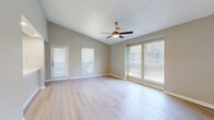 This single-floor residence offers a practical and comfortable layout with two bedrooms, two bathrooms, a living room, kitchen, hallway, and two closets. The living room is a bright, open space highlighted by light-toned hardwood-style flooring, multiple windows with slatted blinds that invite ample natural light, and a ceiling fan with integrated lighting. A separate entry door adds direct access to this welcoming common area. The kitchen is efficiently designed with gray cabinetry, white countertops, stainless steel appliances including a refrigerator, range, and microwave, and matching light hardwood-style flooring that ties the space together. Both bathrooms are finished consistently with gray vanity cabinetry, white countertops, light wood-style flooring, and tiled tub-shower combinations featuring large-format gray tiles for a clean, modern aesthetic. The two bedrooms are carpeted for comfort and each include ceiling fans and closets. The primary bedroom features a sliding-door closet with built-in rods and shelving, while the second bedroom includes a full-width vertical blind covering a sliding door. Neutral gray walls throughout the unit create a cohesive, move-in-ready atmosphere.