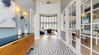 Located at 3100 Van Buren Blvd in Riverside, CA, this thoughtfully designed single-floor space offers a seamless blend of modern elegance and functional layout. The entry hallway immediately impresses with its soaring double-height ceilings and striking geometric patterned tile flooring, setting a sophisticated tone. A warm wood credenza with a dark countertop anchors the entry, complemented by glass-paneled French doors that invite natural light throughout.

The combined living and dining room serves as the heart of the space, featuring expansive floor-to-ceiling windows that frame outdoor views and flood the interior with natural light. A sleek see-through fireplace with light tile surround divides the seating areas, while built-in banquette seating with bold blue upholstery and textured stone accent walls add architectural depth and character. Light hardwood flooring flows continuously through the open-plan area.

The kitchen is efficiently designed with warm wood cabinetry, crisp white quartz countertops, a marble-look tile backsplash, open shelving, and a window overlooking the outdoors — offering both style and practicality. Pendant lighting adds a refined finishing touch. Together, these spaces create a cohesive, well-appointed environment ideal for both gathering and everyday use.