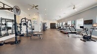 This state-of-the-art fitness center, located at 2130 Mayport Rd in Jacksonville, FL, offers an impressive 1490 square feet of dedicated exercise space. The facility boasts a thoughtful design with high ceilings and multiple ceiling fans, ensuring proper ventilation and comfort during workouts. Large windows line the walls, allowing abundant natural light to flood the space and create an energizing atmosphere.

The gym is equipped with a diverse range of modern fitness apparatus, catering to various workout preferences. A robust strength training area features a multi-station cable machine, free weights, and a comprehensive dumbbell rack. For cardiovascular exercise, the center provides several treadmills, elliptical machines, and stationary bikes, all facing the windows for an enjoyable view during workouts.

The layout is well-organized, with clearly defined zones for different types of exercises. A functional training area includes suspension trainers, stability balls, and other versatile equipment. The flooring appears to be a durable, shock-absorbing material suitable for high-impact activities.

Aesthetically, the space maintains a clean, professional look with a calming color scheme of white walls accented by soft blue tones. Motivational artwork and a branded logo add character to the environment. This fitness center combines functionality with a welcoming ambiance, providing an ideal setting for members to pursue their health and fitness goals.