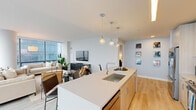 This thoughtfully designed 2-bedroom, 2-bathroom residence at 325 Huguenot St in New Rochelle, NY offers a sleek, modern living experience across a single, well-appointed floor. The open-concept layout connects the kitchen, dining, and living areas seamlessly, creating an expansive, airy atmosphere ideal for both everyday living and entertaining.

The kitchen is a standout feature, showcasing light wood cabinetry, stainless steel appliances, and a large white quartz waterfall island with an undermount sink and bar seating. Globe pendant lights add a stylish accent overhead, while light hardwood flooring runs throughout, lending warmth to the modern aesthetic.

The living room is defined by dramatic floor-to-ceiling windows that wrap the space, flooding it with natural light and offering sweeping urban views of New Rochelle. A structural column adds architectural character to the bright, open room.

The generously sized primary bedroom features soft blue-gray walls, large windows with city views, and light hardwood flooring, creating a calm and restful retreat. The second bedroom is equally well-lit, with its own window view and refined finishes.

Both bathrooms are finished with light wood vanities and clean white countertops. The primary bath features large-format gray marble-style tile surrounding a soaking tub with an integrated shower, while the second bath maintains the same refined, contemporary style.