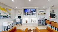 Located at 1901 Brown St in El Paso, Texas, this thoughtfully designed single-floor space offers a well-appointed, multifunctional layout that balances style with practicality. Light beige tile flooring runs throughout, complementing the neutral gray walls and textured ceiling fitted with recessed lighting that keeps the interior bright and inviting.

The main lounge area serves as the heart of the space, anchored by cognac leather seating and a decorative coffee table. A striking built-in wall unit frames a large flat-screen television above two illuminated display niches, adding an elegant architectural focal point. To one side, a compact marble-topped desk with a monitor provides a functional workstation, while a vibrant abstract painting adds a lively burst of color to the walls.

A dedicated café corner features an open shelving unit stocked with coffee essentials, positioned near French doors that flood the area with natural light and offer a view of the outdoors. Adjacent to this, a dining nook with a round table and chairs provides a casual seating option.

The kitchenette is efficiently arranged with granite countertops, a stainless steel sink, a refrigerator, microwave, and a hanging wine glass rack, making it well-equipped for light hospitality needs. A wall-mounted mini-split unit ensures year-round climate comfort. Together, these elements create a polished, welcoming environment suited for a variety of uses.