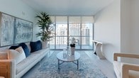 This contemporary single-floor residence at 49I offers a bright, open layout defined by clean lines and a crisp white palette throughout. The living area is a standout feature, anchored by expansive floor-to-ceiling windows and sliding glass doors that flood the space with natural light and frame sweeping views of the surrounding urban skyline. Light wood-tone flooring flows seamlessly throughout, enhancing the airy, modern ambiance.

The kitchen is thoughtfully designed with high-gloss white cabinetry, dark stone countertops, a central island, and a full suite of stainless steel Bosch appliances, including a built-in oven, microwave, and a large French-door refrigerator. Recessed and pendant lighting adds both function and style.

The bedroom continues the minimalist aesthetic, featuring the same light flooring and direct access to the balcony through floor-to-ceiling glazing, offering unobstructed city views.

The bathroom is finished to a high standard, showcasing marble-look tile flooring, a wide vanity with white quartz countertop, chrome fixtures, a large illuminated mirror, and a separate louvered storage closet. The overall design of this residence reflects a polished, contemporary style with an emphasis on natural light, open space, and refined finishes throughout.