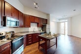 Located at 9142 Richmond Hwy in Fort Belvoir, Virginia, this well-appointed one-bedroom, one-bathroom residence offers a thoughtfully designed single-floor layout with a comfortable and functional living experience. Rich hardwood flooring flows throughout the main living areas, creating a warm and cohesive aesthetic from the kitchen through to the open living space.

The kitchen is a standout feature, showcasing deep cherry wood cabinetry that extends to the ceiling for ample storage, granite countertops, and a full suite of stainless steel appliances including a gas range, microwave, and refrigerator. A central kitchen island provides additional prep and dining space, seamlessly connecting to the open living and dining area, which is bathed in natural light from a glass patio door.

The generously sized bedroom features plush carpeting, soaring ceilings, a ceiling fan, and natural light from a large window. It is complemented by a dedicated walk-in closet and additional closet storage, offering notable organizational flexibility. The clean, bright bathroom includes a full soaking tub and shower combination with white tile surround and granite-topped vanity.

Additional highlights include a private patio, in-unit laundry, and three closets throughout. The neutral color palette and modern finishes contribute to a bright, move-in-ready ambiance throughout the space.