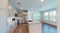 Located at 2620 Mall of Georgia Blvd in Buford, GA, this well-appointed single-floor residence combines modern design with functional living. The open-concept kitchen serves as the heart of the home, showcasing a large central island with a granite countertop and undermount sink, complemented by shaker-style cabinetry, a full suite of stainless steel appliances, and a classic tile backsplash. Natural light pours in through multiple windows, offering pleasant views of surrounding greenery. Wood-look plank flooring extends throughout the main living areas, providing a warm and cohesive aesthetic. The bedrooms offer comfortable retreats — one features a wall of windows for abundant natural light and hardwood-style flooring, while another is carpeted and includes a ceiling fan. The bathrooms are finished with granite-topped vanities, gold-accented hardware, and large mirrors. One bathroom features a dual-sink vanity and a spacious walk-in layout leading to a dedicated closet. Additional highlights include a built-in shelving and workspace area ideal for storage or a home office, as well as an in-unit stacked washer and dryer. The clean, neutral palette and recessed lighting throughout create a bright and modern atmosphere.