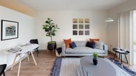 Located at 10720 5th Avenue NE in Seattle's Pinehurst neighborhood, this thoughtfully designed single-floor unit offers a clean, modern aesthetic throughout. The open-concept layout connects the living and kitchen areas seamlessly, with warm wood-tone flooring running through the main spaces and bringing a sense of continuity to the design.

The kitchen is a standout feature, showcasing two-tone cabinetry with dark lower cabinets and crisp white upper cabinets, white quartz countertops, and a full suite of stainless steel appliances including a range, over-the-range microwave, dishwasher, and refrigerator. A peninsula provides additional prep space and casual seating potential.

The living area is bright and welcoming, enhanced by large sliding glass doors that open to a private balcony with views of the surrounding neighborhood, allowing natural light to fill the room. The bedroom offers a cozy, well-proportioned retreat with wall-mounted shelving and soft, warm lighting. The bathroom features stone-look tile flooring, a dark vanity with white countertop, and an accessible layout. A dedicated laundry area with a stacked washer and dryer adds everyday convenience. Light wood flooring and neutral walls contribute to the unit's clean, contemporary character throughout.