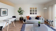 Located at 10720 5th Avenue NE in Seattle's Pinehurst neighborhood, this thoughtfully designed single-floor unit offers a clean, modern aesthetic throughout. The open-concept layout connects the living and kitchen areas seamlessly, with warm wood-tone flooring running through the main spaces and bringing a sense of continuity to the design.

The kitchen is a standout feature, showcasing two-tone cabinetry with dark lower cabinets and crisp white upper cabinets, white quartz countertops, and a full suite of stainless steel appliances including a range, over-the-range microwave, dishwasher, and refrigerator. A peninsula provides additional prep space and casual seating potential.

The living area is bright and welcoming, enhanced by large sliding glass doors that open to a private balcony with views of the surrounding neighborhood, allowing natural light to fill the room. The bedroom offers a cozy, well-proportioned retreat with wall-mounted shelving and soft, warm lighting. The bathroom features stone-look tile flooring, a dark vanity with white countertop, and an accessible layout. A dedicated laundry area with a stacked washer and dryer adds everyday convenience. Light wood flooring and neutral walls contribute to the unit's clean, contemporary character throughout.