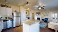 Located at 1001 E 1st Ave in Broomfield, Colorado, this single-floor residence offers a thoughtfully designed layout with a seamless flow between its main living areas. The kitchen is outfitted with stainless steel appliances, white cabinetry, a subway tile backsplash, granite countertops, and a center island, all set atop warm hardwood-style flooring. The open-concept design connects the kitchen directly to a bright dining area surrounded by large windows that flood the space with natural light and offer views of the surrounding neighborhood. The living room is anchored by a white-surround fireplace, crown molding, and a ceiling fan, with a built-in study nook providing a dedicated workspace. A glass-paned door in the living area opens to an outdoor space. The bedrooms feature plush carpeting, generous closet space, ceiling fans, and large windows. The bathroom is well-appointed with granite countertops, white cabinetry, a full tub and shower, and hardwood-style flooring. A dedicated in-unit laundry room with side-by-side washer and dryer and overhead shelving adds everyday convenience. Throughout the residence, neutral warm tones and consistent finishes create a cohesive and comfortable living environment.