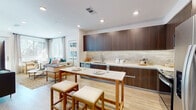 Located at 6200 Sunset Blvd in the heart of Hollywood, this single-floor residence offers a thoughtfully designed open-concept layout with contemporary finishes throughout. Light wood-tone flooring flows seamlessly across the entire unit, complementing the bright, white walls and recessed lighting.

The kitchen is a standout feature, boasting rich dark walnut cabinetry extending to the ceiling, light stone countertops, a neutral tile backsplash, and stainless steel appliances including a range, microwave, and refrigerator. A marble-topped island with bar seating provides additional prep and dining space, while the open layout connects directly to the living area.

The living room is generously proportioned, with corner windows inviting abundant natural light and offering views of surrounding greenery. A private exterior door further enhances accessibility and airflow.

Two well-appointed bedrooms each feature large windows with blinds and ceiling fans. The primary bedroom is served by an en-suite bathroom with a dark wood floating vanity, large wall mirror, and a tub-shower combination. A second full bathroom mirrors the modern aesthetic with similar cabinetry, large-format tile flooring, and a wall-mounted storage cabinet.

A clean, well-lit hallway connects all areas of the home, completing this polished and functional Hollywood residence.