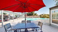 Located at 300 Cirby Hills Dr in Roseville, California, this outdoor community amenity area offers a well-appointed recreational space designed for relaxation and leisure. The centerpiece is a generously sized swimming pool with a distinctive geometric shape, complemented by a built-in spa for year-round enjoyment. The surrounding pool deck provides ample space for sunbathing, furnished with multiple lounge chairs positioned to take advantage of the abundant California sunshine and open sky views.

A pergola structure anchors one side of the pool area, offering a shaded retreat for outdoor dining and gathering. Nearby, a covered patio equipped with a dining table and umbrella extends from the clubhouse building, which features large glass panel doors that create a seamless connection between indoor and outdoor spaces. The clubhouse facade is finished in a clean, neutral palette and serves as a functional backdrop to the outdoor area.

The pool is fully enclosed by a sleek metal security fence with gated access, ensuring both safety and privacy. Mature trees — including towering pines and broad deciduous varieties — frame the perimeter, providing natural shade and a lush, verdant setting. The surrounding landscaping and open sightlines to the adjacent residential buildings contribute to the welcoming, community-centered character of this amenity space.