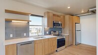 Located in the heart of downtown Salt Lake City at 360 W 200 S, this modern one-bedroom, one-bathroom unit offers a thoughtfully designed open-concept layout with clean lines and contemporary finishes throughout. Light hardwood flooring flows seamlessly across the entire space, complementing the bright, neutral palette.

The combined living, dining, and kitchen area serves as the centerpiece of the unit. The kitchen is outfitted with natural wood cabinetry, white quartz countertops, a blue-gray tile backsplash, and a full suite of stainless steel appliances including a refrigerator, range, microwave, and dishwasher. A large window above the sink frames sweeping city and mountain views, flooding the space with natural light.

The living area is anchored by expansive floor-to-ceiling windows and sliding glass panels that offer panoramic views of the Salt Lake City skyline and the Wasatch Range beyond. Exposed ductwork adds an industrial design touch alongside track lighting overhead.

The bedroom is a serene retreat with a window overlooking the cityscape and a spacious closet with sliding doors. The bathroom features light hardwood flooring, a soaking tub, and a tiled shower surround with a built-in niche. A dedicated laundry area with a stacked washer and dryer rounds out this well-appointed urban residence.