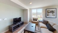 Located at 151 Andover Park E in Tukwila, WA, this well-appointed upper-floor unit offers a thoughtfully designed layout with modern finishes throughout. The open-concept kitchen is a standout feature, showcasing rich dark wood cabinetry, granite countertops with a tile backsplash, a full suite of stainless steel appliances, and a central island with seating — ideal for both cooking and casual dining. Light wood-style flooring flows throughout the main living areas, creating a warm, cohesive aesthetic.

The sun-filled dining area is framed by large corner windows that invite abundant natural light and offer sweeping views of the Tukwila cityscape and surrounding greenery. Adjacent to the dining space, the living room provides a comfortable gathering area with equally impressive window views.

The unit features two well-sized bedrooms, each carpeted and outfitted with ceiling fans and generous windows that continue the theme of natural light and outdoor views. The hallway connecting the rooms features clean, neutral walls with consistent wood-style flooring.

The bathroom is finished with the same granite countertop detailing seen in the kitchen, complemented by dark wood cabinetry, wood-style flooring, and a shower-tub combination. The overall design is clean, modern, and move-in ready.