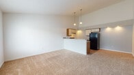 Located at 1738 SR-303 in Streetsboro, Ohio, this single-floor unit offers a well-organized layout designed for comfortable everyday living. The open-concept living area is a standout feature, characterized by soaring vaulted ceilings that lend an airy, expansive feel to the space. Neutral-toned carpet extends throughout the living area and bedrooms, contributing to a clean and cohesive aesthetic.

The kitchen is positioned adjacent to the living area, separated by a peninsula-style breakfast bar with a warm wood-accented base. The kitchen itself features hardwood-style flooring, cream-colored cabinetry with wood trim, ample counter space, and black appliances including a refrigerator, dishwasher, and a gas range with an overhead ventilation hood. Pendant lighting above the kitchen area adds a decorative touch while enhancing functionality.

The bedrooms are generously sized, each with plush carpeting and bright white walls. The primary bedroom includes a walk-in closet as well as an additional closet, offering substantial storage. A secondary bedroom features a wide window that allows natural light to fill the room. The bathroom is equipped with a full tub-shower combination, hardwood-style flooring, and a vanity with a mirror. The overall palette throughout the unit is light and neutral, creating a bright and welcoming atmosphere.
