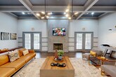 Located at 4025 Oakwood Dr in Chattanooga, TN, this single-floor space delivers a refined and welcoming atmosphere across a thoughtfully designed layout. The living room serves as the centerpiece, boasting dramatic coffered ceilings with dark inset panels, rich hardwood flooring, and a striking floor-to-ceiling stone tile fireplace flanked by two sets of French doors that invite abundant natural light. A contemporary multi-arm pendant light fixture adds a modern touch overhead, while the generous proportions of the room create an open and airy feel. An arched passageway leads seamlessly into additional areas, including a dining room that features a softly striped accent wall, natural light from a large window, and stylish modern lighting. The kitchen is equipped with an extended quartz countertop, sage-toned cabinetry with matte black hardware, a double stainless steel sink, open wooden floating shelves, and a textured tile backsplash. Hardwood flooring flows consistently throughout the space, tying each room together cohesively. The overall design balances classic architectural details with contemporary finishes, resulting in a space that is both functional and visually engaging.