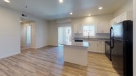 This single-floor residence offers a clean, modern design with a thoughtful layout that balances open communal spaces and private quarters. The heart of the home is an open-concept kitchen and living area finished with light hardwood-style flooring that extends throughout the main living spaces. The kitchen is well-equipped with crisp white shaker cabinetry, granite countertops, a suite of black appliances including a range, microwave, dishwasher, and refrigerator, and a central island that provides additional prep space and serves as a natural gathering point. Recessed lighting illuminates the area, while a sliding glass door and adjacent window invite natural light and provide access to the exterior. The bedrooms feature neutral wall-to-wall carpeting and clean white walls, creating a calm and versatile environment. Window blinds offer privacy while still allowing natural light to filter in. The two full bathrooms are finished consistently, each featuring warm beige tile flooring, white vanities with granite countertops, and a tub-shower combination unit. The overall aesthetic throughout the home is cohesive and neutral, emphasizing clean lines, light tones, and functional finishes that provide a move-in-ready foundation.