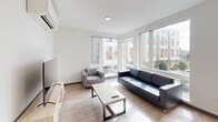 Located at 4759 15th Ave NE in Seattle's University District, this modern single-floor unit offers five bedrooms, four bathrooms, and a thoughtfully designed layout that maximizes every square foot. The interior features a clean, contemporary aesthetic with light wood-tone flooring, crisp white walls, and an abundance of natural light throughout.

The living room is a bright, welcoming space anchored by large corner windows that frame views of the surrounding neighborhood, filling the room with daylight. A wall-mounted mini-split system provides efficient climate control, and the space comfortably accommodates a full seating arrangement and entertainment setup.

The kitchen is outfitted with light wood cabinetry, stone-look countertops, stainless steel appliances including a full-size refrigerator, and a tall window that draws in generous natural light. Each of the five bedrooms is a private, well-proportioned room with keypad-secured entry doors for added privacy and security.

The four bathrooms are finished with light wood vanities, white quartz countertops, and clean tile work, with some featuring tub-shower combinations. A dedicated laundry room houses a full-size Whirlpool washer and dryer. Three hallways connect the rooms efficiently, rounding out a functional and modern living environment.