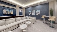 This contemporary lounge is thoughtfully designed to accommodate both relaxed gatherings and casual social interaction. The space is anchored by a large, plush light-gray sectional sofa arranged around a pair of sleek marble-topped coffee tables, creating an inviting central seating area. A wall-mounted flat-screen television is set against a striking deep-blue textured accent wall, flanked by elegant wall sconces that cast a warm, ambient glow throughout the room.

The architectural design incorporates a coffered ceiling with integrated LED cove lighting, adding depth and a refined sense of sophistication to the overall aesthetic. Structural columns dressed in contrasting white and blue paneling define the room's layout while contributing to its contemporary character. Complementing the main seating area, a high-top bistro table with chrome-based swivel chairs offers an alternative casual seating option.

The flooring features a herringbone-patterned carpet in neutral gray tones, tying the design elements together cohesively. Curated wall art in blue and white tones echoes the room's color palette, while potted decorative plants introduce organic texture. Recessed lighting supplements the ambient fixtures, ensuring the space is well-lit and welcoming throughout.