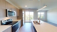 This single-story residence showcases a clean, contemporary design throughout its well-appointed spaces. The galley-style kitchen is a functional highlight, featuring warm wood-tone cabinetry extending to the ceiling, light quartz countertops, a subway tile backsplash, and a full suite of stainless steel appliances including a refrigerator, electric range, over-the-range microwave, and dishwasher. A large kitchen island with an undermount double sink and pendant lighting serves as a natural dividing point between the kitchen and the open living area. A sliding glass door leads directly from the kitchen to a private balcony, flooding the space with natural light and offering views of surrounding greenery.

The living area is bright and open, benefiting from additional windows that frame outdoor views. Bedrooms are generously sized, with plush carpeting and large windows. The primary bathroom includes a dual-sink vanity with quartz countertops, wood-tone cabinetry, and a large mirror, while a secondary bathroom offers a tub-shower combination. A dedicated laundry room houses a full-size side-by-side washer and dryer, adding everyday convenience to this thoughtfully designed residence.
