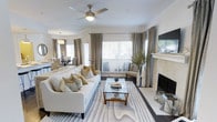 This single-floor residence is thoughtfully designed with a flowing, open layout that connects its key living areas seamlessly. The living room serves as the heart of the home, featuring a fireplace with a classic white mantel, a ceiling fan, and multiple windows dressed in layered neutral drapes that allow generous natural light to fill the space. The room comfortably accommodates generous seating and is anchored by a patterned area rug that complements the warm, neutral tones found throughout.

Adjacent to the living room, a dedicated dining area provides a formal setting for meals, while the kitchen is centrally positioned within the floor plan, offering an efficient workspace with ample cabinetry and counter space. The layout suggests a clear separation between the social and private areas of the home, with bedroom spaces positioned toward one end of the residence.

Throughout the home, a consistent design language of soft whites, warm beiges, and subtle gold accents creates a refined and cohesive ambiance. Hard flooring runs through the main areas, adding durability and visual continuity. The overall atmosphere is bright, well-organized, and welcoming, with attention to detail evident in each room's furnishings and finishes.
