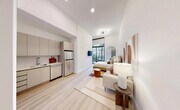 Located at 640 NW 7th Ave in Fort Lauderdale, FL, this modern studio is thoughtfully designed to maximize every square foot with a clean, open-concept layout. Soaring ceilings amplify the sense of space throughout, while light oak hardwood flooring and bright white walls create a warm, contemporary aesthetic.

The kitchen is efficiently integrated into the main living area and features flat-front cabinetry in a soft taupe finish, stainless steel appliances including a full-size refrigerator and dishwasher, and a sleek single-basin sink. The living and sleeping area flows seamlessly beyond the kitchen, anchored by an elegant arched accent wall that frames the bedroom zone. Large floor-to-ceiling windows and a private balcony flood the interior with natural light and offer a lush outdoor view.

The full bathroom is finished in neutral tones with a floating vanity, an undermount sink, and a combined tub and shower with a rain showerhead. Additional conveniences include two closets — one with louvered doors — a dedicated laundry area, and a utility room. The overall ambiance is sophisticated yet approachable, blending modern design with practical functionality in the heart of Fort Lauderdale.